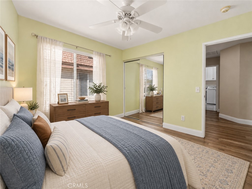 Another View Of The Bedroom Highlighting The Mirrored Closet Doors, Ceiling Fan, Wood-Look Flooring, And Large Window With Soft Window Treatments. Digitally Staged