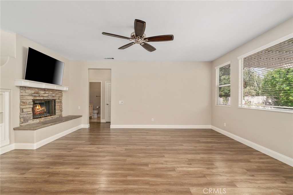 Another View Of The Spacious Family Room Highlighting The Beautiful Stone-Surround Fireplace, Wood-Look Flooring, Ceiling Fan, And Abundant Natural Light.