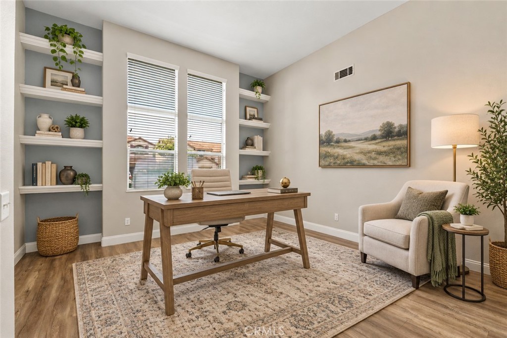 Versatile Front Room Featuring Built-In Shelving, Wood-Look Flooring, And Abundant Natural Light, Beautifully Arranged As A Home Office. Digitally Staged