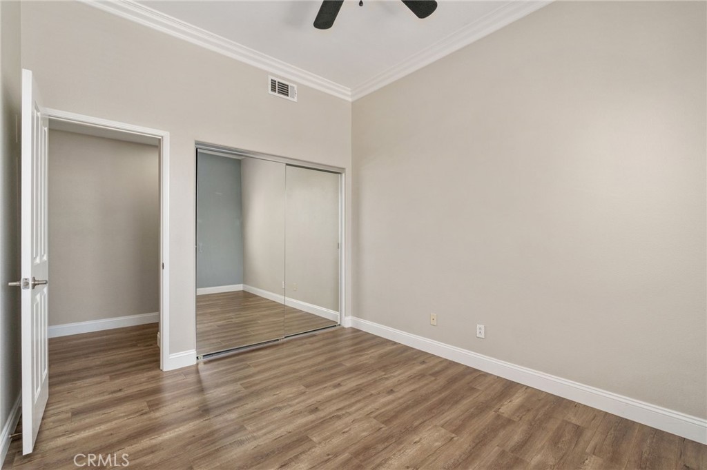 Another View Of The Secondary Bedroom Highlighting The Mirrored Closet Doors, Elegant Crown Molding, Generous Floor Space, And Attractive Wood-Look Flooring.