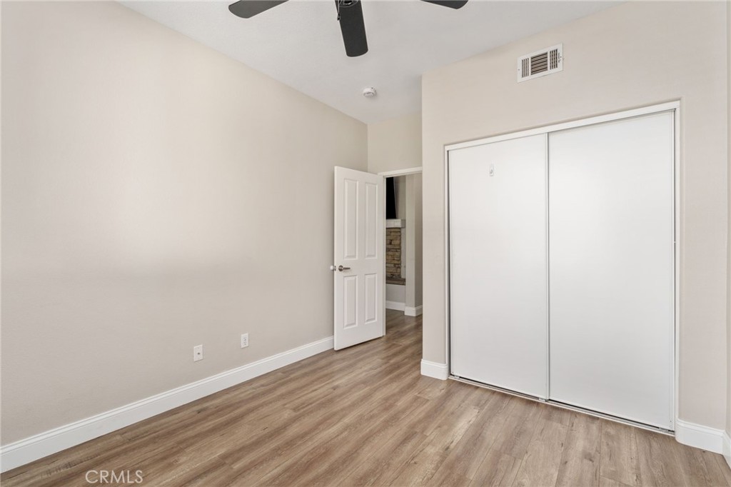 Another View Of The Bedroom Highlighting The Spacious Layout, Sliding-Door Closet, Ceiling Fan, And Attractive Wood-Look Flooring.