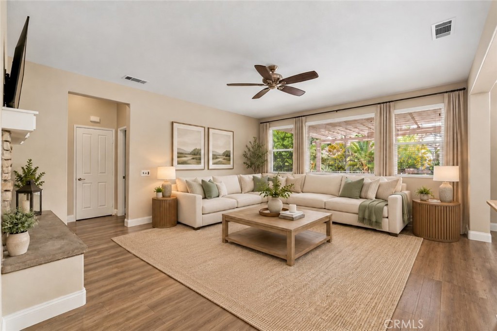 Inviting Family Room Featuring Wood-Look Flooring, A Ceiling Fan, And Large Windows Overlooking The Backyard, Creating A Comfortable Space For Relaxation And Entertaining. Digitally Staged