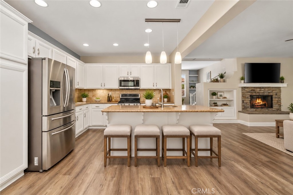 Spacious Open-Concept Kitchen Featuring A Large Center Island With Breakfast Bar Seating, Stainless Steel Appliances, Recessed Lighting, And A Beautiful View Into The Family Room With Stone-Surround Fireplace. Digitally Staged
