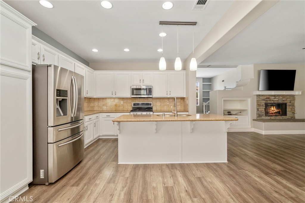 Spacious Open-Concept Kitchen Featuring A Large Center Island With Breakfast Bar, Stainless Steel Appliances, Recessed Lighting, And A Beautiful View Into The Family Room With Stone-Surround Fireplace.
