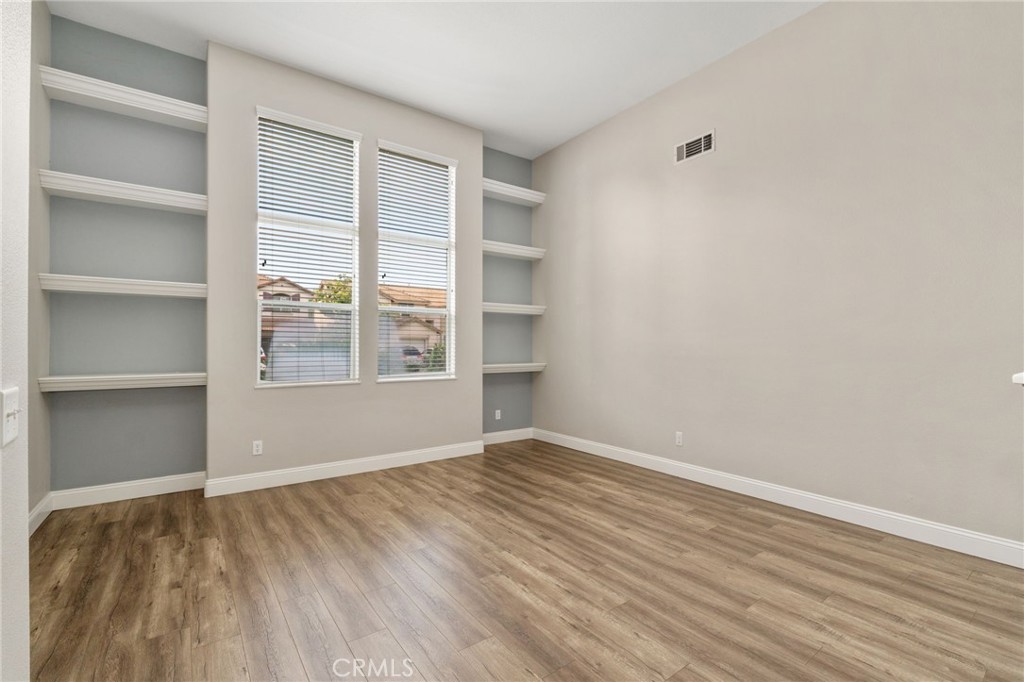 Spacious And Versatile Front Room Featuring Built-In Shelving, Large Windows, And Wood-Look Flooring, Offering Endless Possibilities For A Home Office, Sitting Room, Or Additional Living Area.