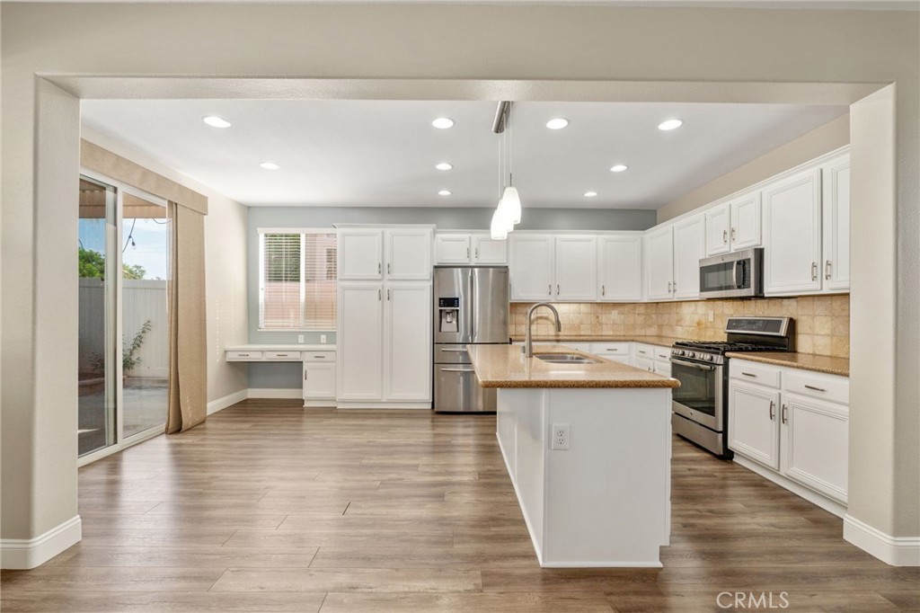 Spacious Kitchen And Adjacent Dining Area Featuring White Cabinetry, Stainless Steel Appliances, A Large Center Island, Recessed Lighting, And Sliding Glass Door Access To The Backyard.