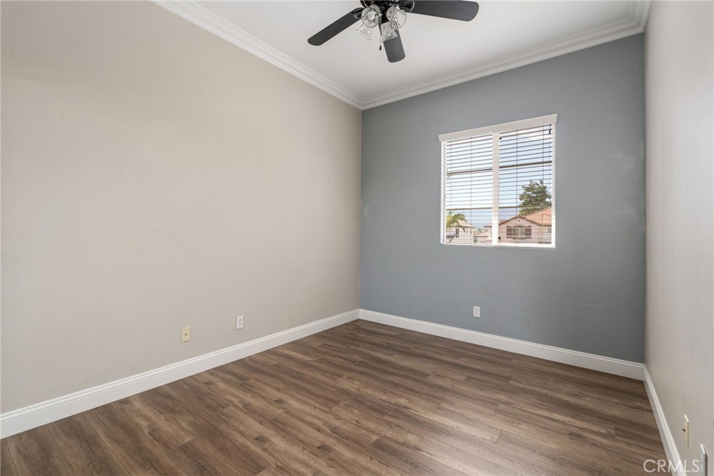 Spacious Secondary Bedroom Featuring An Attractive Accent Wall, Crown Molding, Ceiling Fan, Wood-Look Flooring, And A Large Window Providing Natural Light.