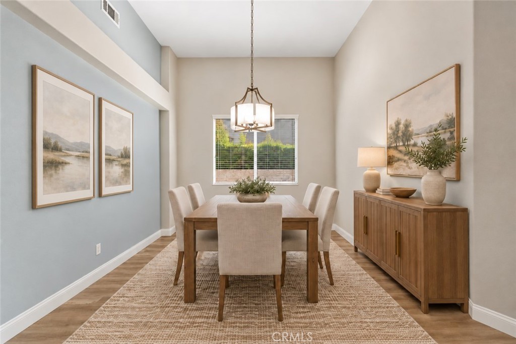 Elegant Formal Dining Room Featuring Soaring Ceilings, An Attractive Light Fixture, Wood-Look Flooring, And A Large Window Providing Natural Light. Digitally Staged