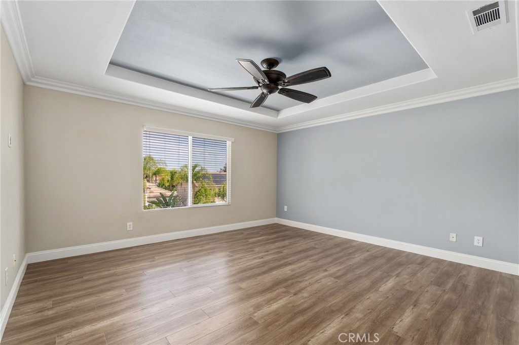 Beautiful Primary Suite Featuring A Decorative Tray Ceiling With Crown Molding, Ceiling Fan, Attractive Wood-Look Flooring, And A Large Window Providing Abundant Natural Light.