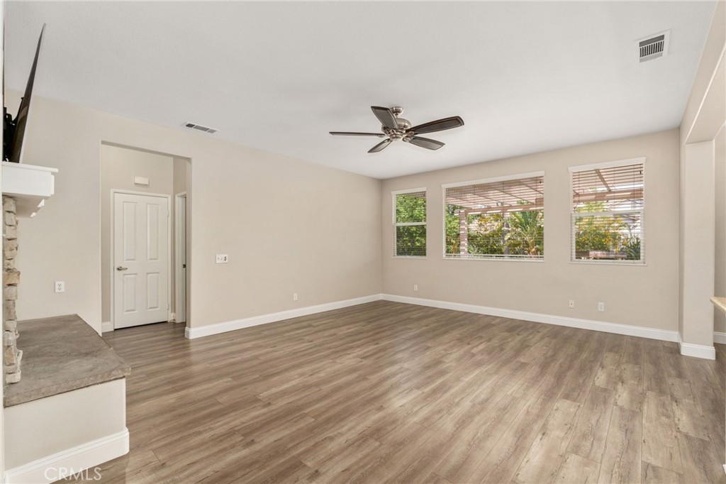 Inviting Family Room Featuring Wood-Look Flooring, A Ceiling Fan, And Large Windows Overlooking The Backyard, Creating A Comfortable Space For Relaxation And Entertaining.