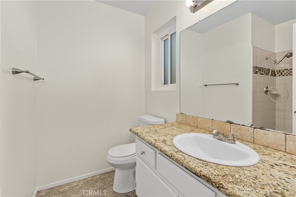 Primary bathroom featuring a granite-topped vanity, single sink, and tiled shower with decorative mosaic accents.