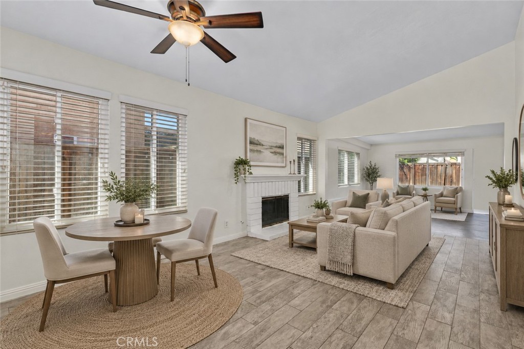 Bright and inviting living and dining areas featuring wood-look flooring, a cozy fireplace, and an open connection to the enclosed patio. Digitally Staged Bright and inviting living and dining areas featuring wood-look flooring, a cozy fireplace, and an open connection to the enclosed patio. Digitally Staged