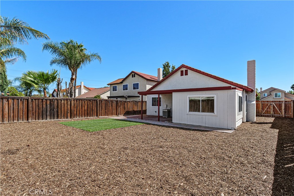 Another backyard perspective highlights the open outdoor space, perimeter fencing, and mature palm trees beyond the property