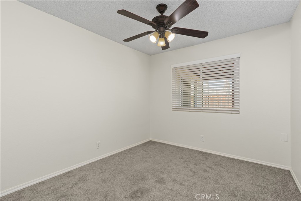 Secondary bedroom offering soft carpeting, a ceiling fan, and a window bringing natural light into the space.
