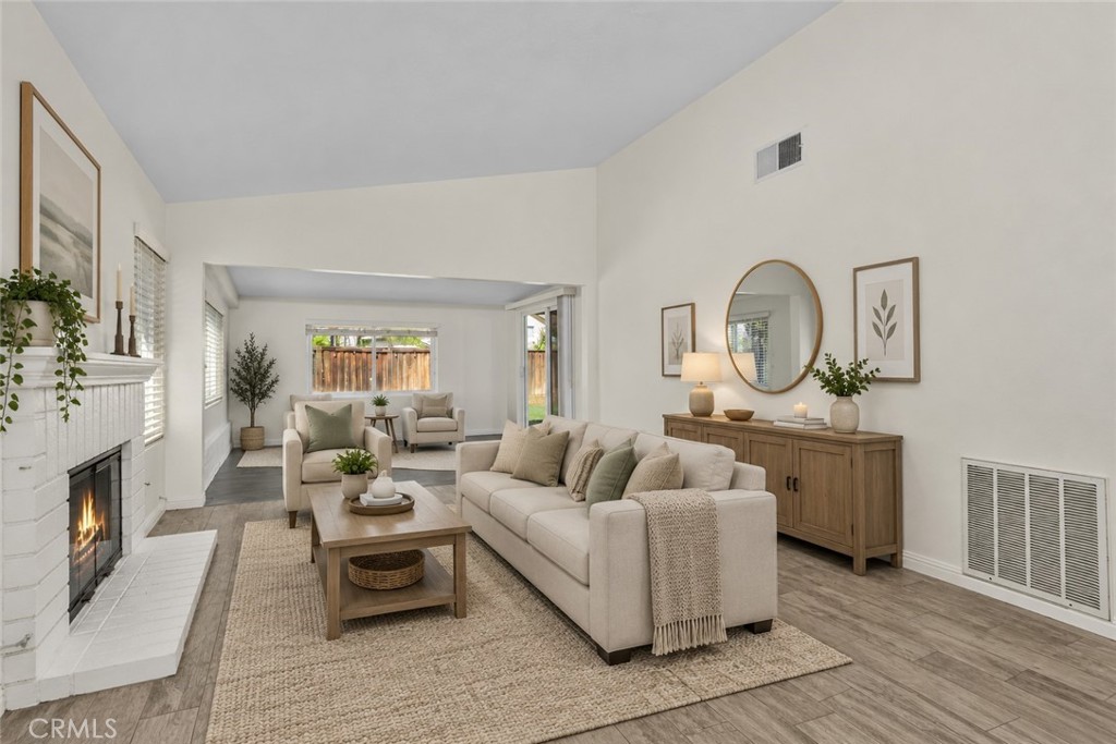 Spacious living area featuring a charming white brick fireplace, generous natural light, and an open layout extending toward the enclosed patio. Digitally Staged Spacious living area featuring a charming white brick fireplace, generous natural light, and an open layout extending toward the enclosed patio. Digitally Staged
