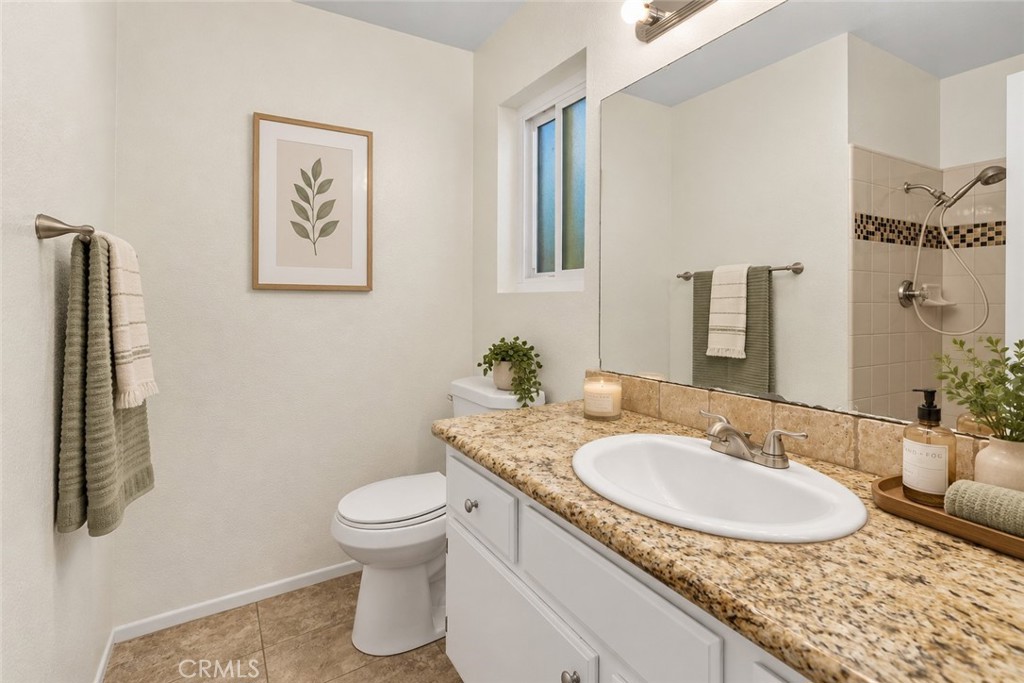 Primary bathroom featuring a granite-topped vanity, single sink, and tiled shower with decorative mosaic accents. Digitally Staged