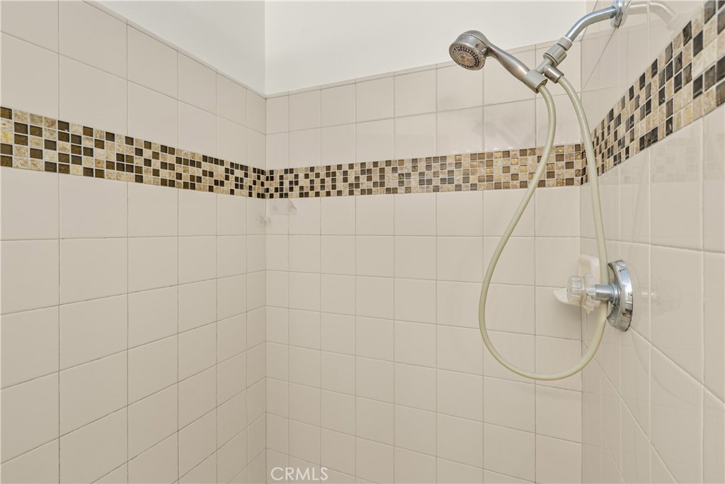 A closer look at the primary bathroom shower featuring a tiled surround, decorative mosaic accents, and a handheld showerhead.