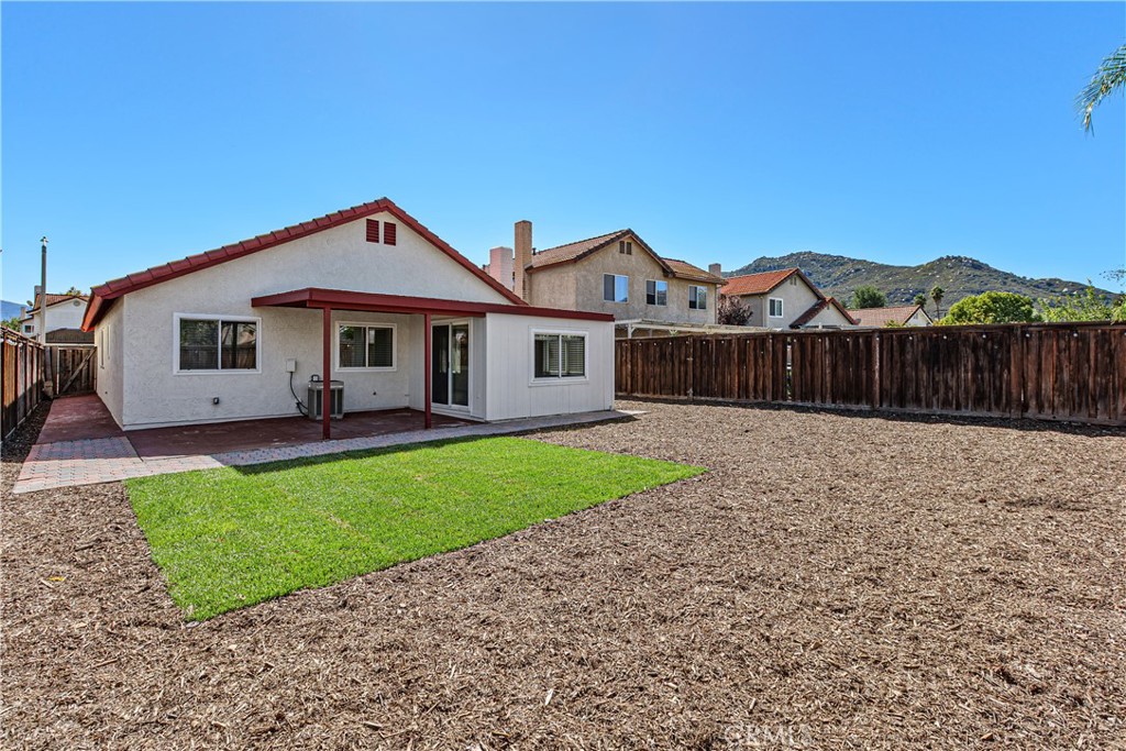 Rear exterior view showcasing the covered patio, green lawn area, and low-maintenance landscaping within the fenced backyard.