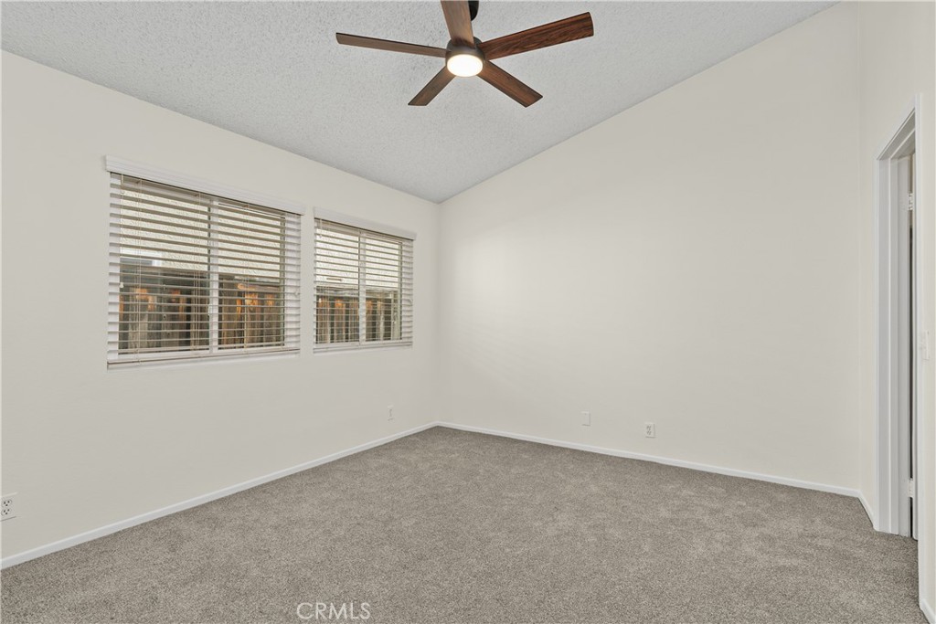 The comfortable primary bedroom features soft carpeting, a ceiling fan, and two windows providing natural light.