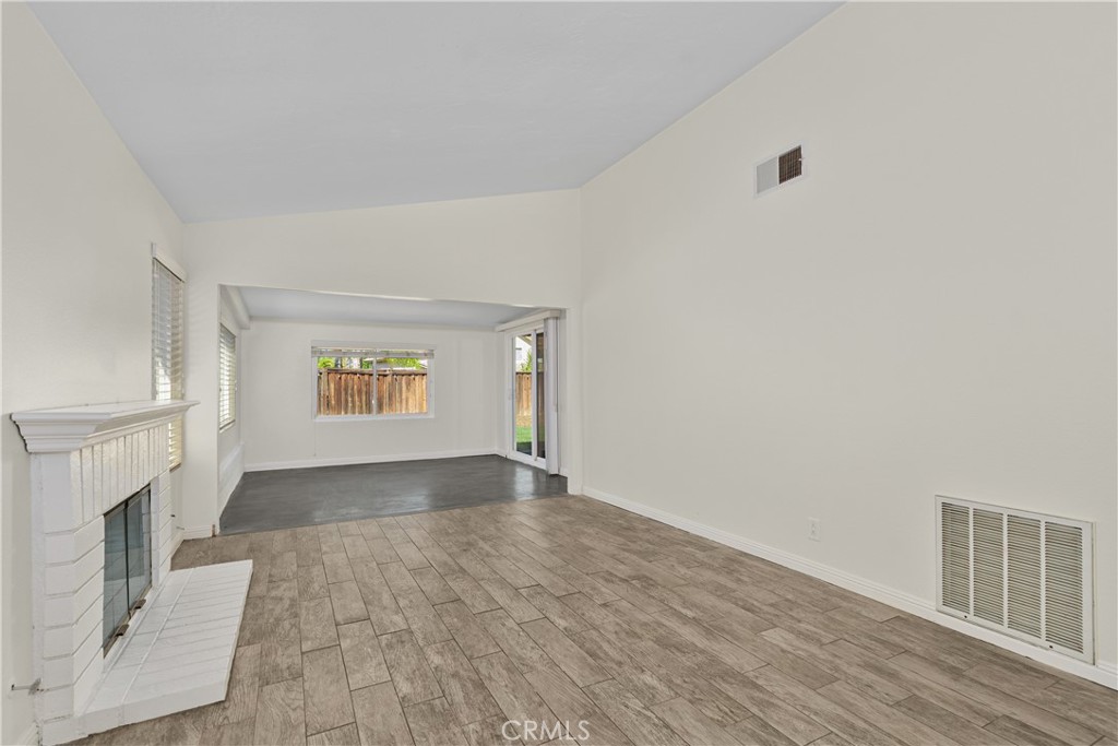 Spacious living area featuring a charming white brick fireplace, generous natural light, and an open layout extending toward the enclosed patio. Spacious living area featuring a charming white brick fireplace, generous natural light, and an open layout extending toward the enclosed patio.
