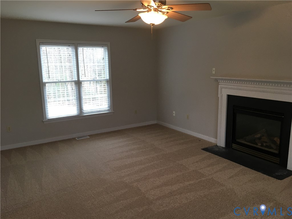 Unfurnished living room with light carpet, ceiling fan, and a fireplace with flush hearth