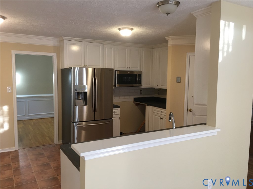 Kitchen with appliances with stainless steel finishes, crown molding, white cabinets, a textured ceiling, and decorative backsplash