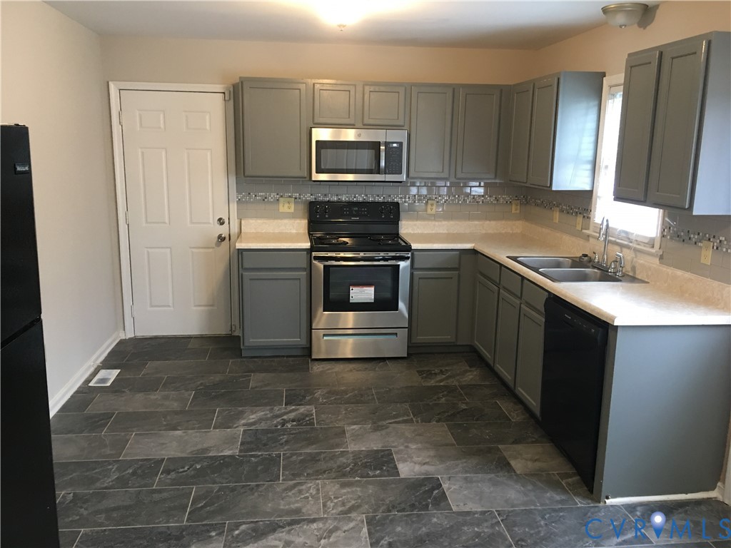 Kitchen with gray cabinets, black appliances, light countertops, and decorative backsplash Kitchen with gray cabinets, black appliances, light countertops, and decorative backsplash