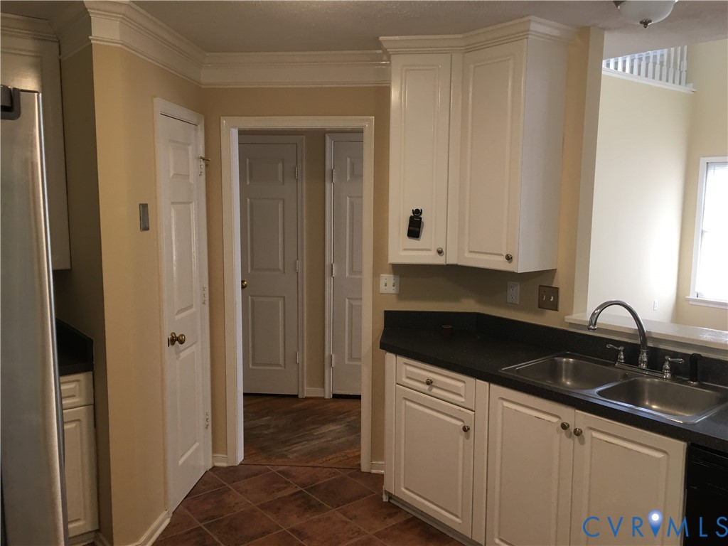 Kitchen featuring dark countertops, white cabinets, dark tile patterned floors, black dishwasher, and ornamental molding
