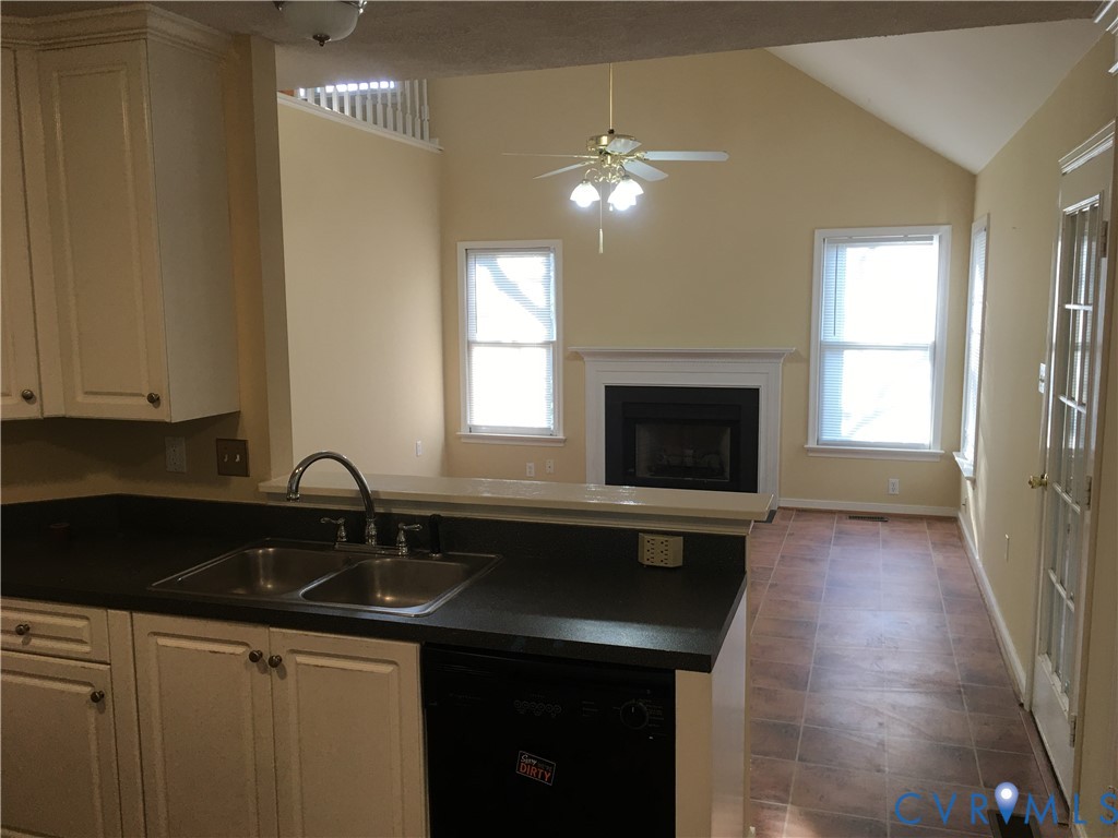 Kitchen with dark countertops, dishwasher, vaulted ceiling, healthy amount of natural light, and a fireplace