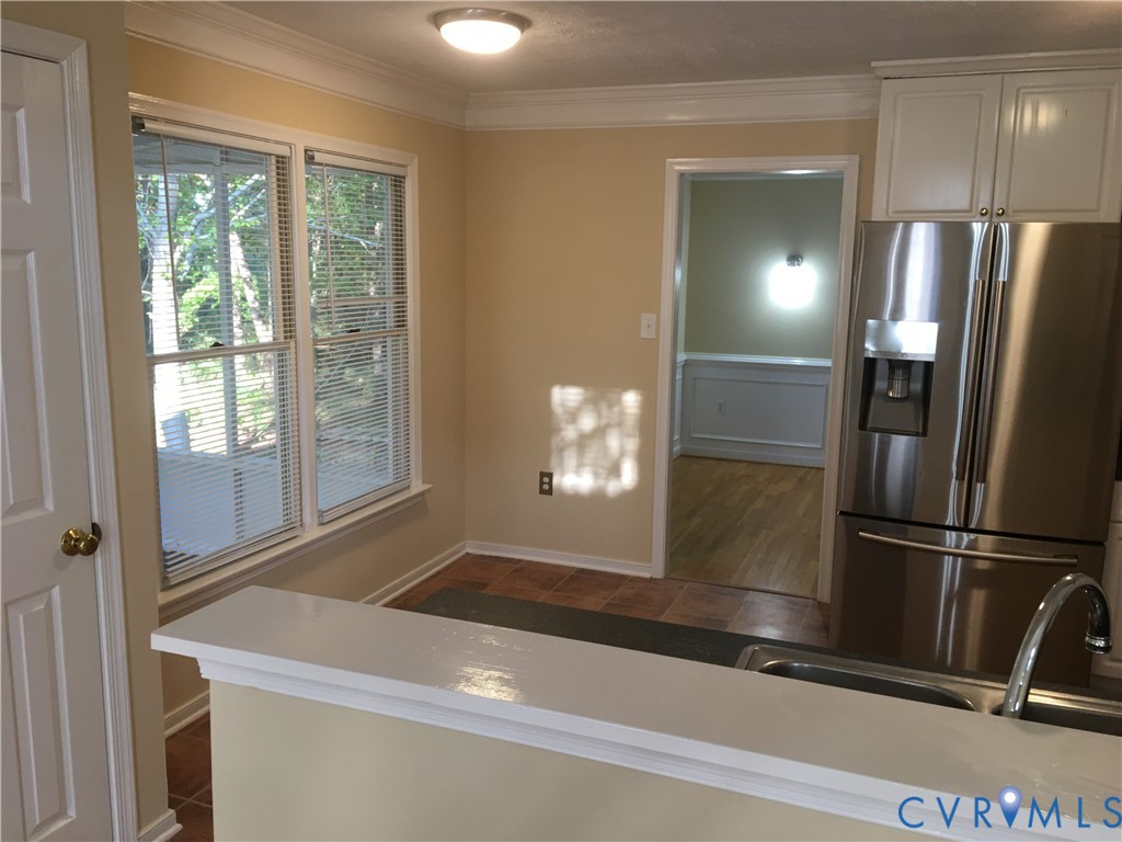 Kitchen featuring stainless steel fridge, ornamental molding, light countertops, and white cabinetry