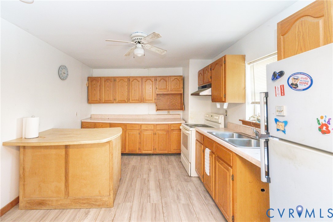 Kitchen with white appliances, light countertops, a ceiling fan, and light wood-style floors