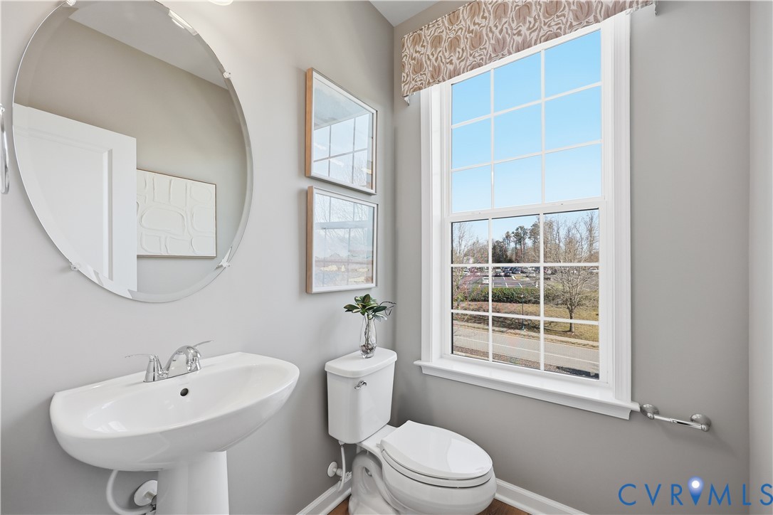 Bathroom featuring a pedestal sink, round mirror, and a window with a patterned valance