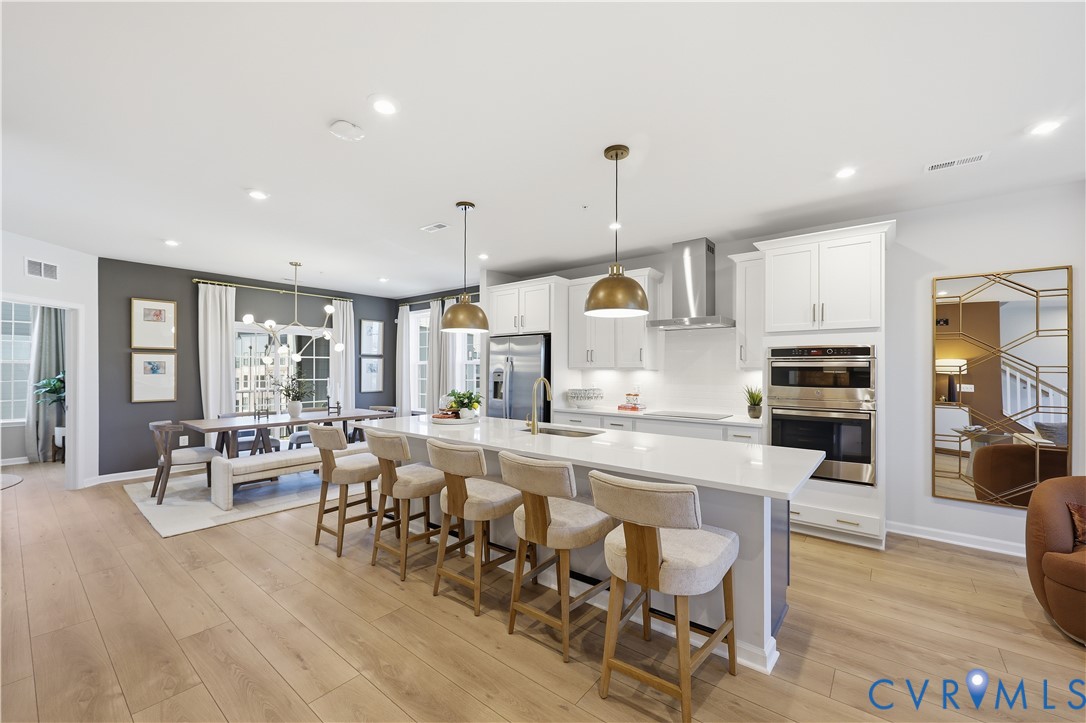 Open-concept kitchen and dining area featuring light wood-finish flooring, a spacious island with a light-toned countertop, white cabinetry, stainless steel appliances, and recessed lighting