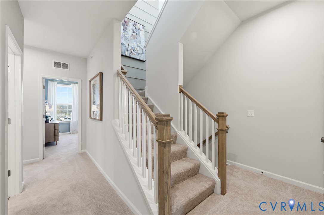 Carpeted staircase with wood-finish handrails and white balusters