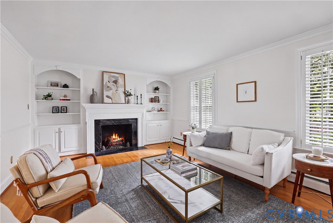 Fireplace featuring a dark stone surround and decorative mantle, flanked by built-in arched cabinetry with shelving, wood-finish flooring, and window shutters