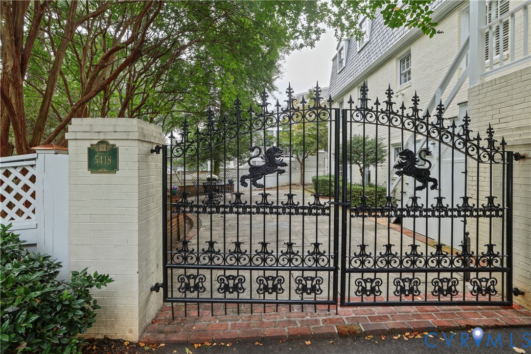 Gated entrance featuring ornate wrought-iron double doors, brick-bordered stone paved courtyard, and painted brick exterior walls