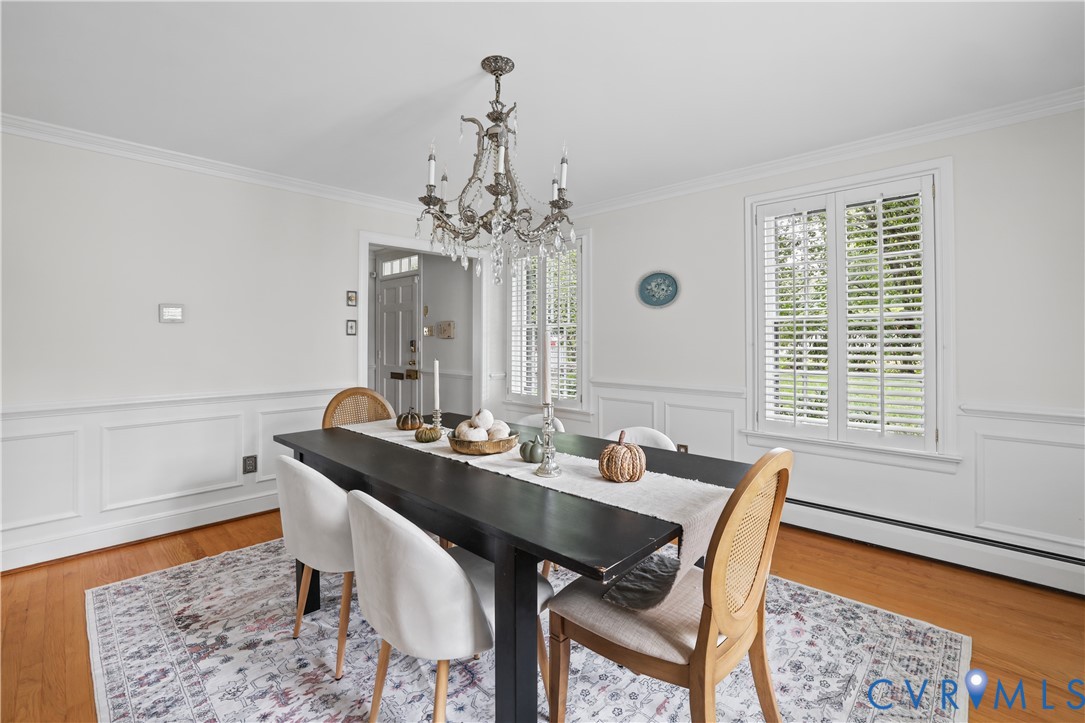 Dining area featuring wainscoting, wood-finish flooring, a tiered crystal chandelier, and shuttered windows