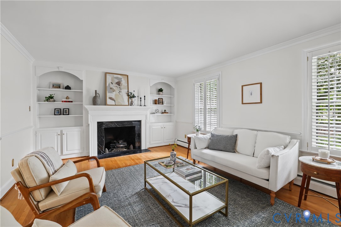 Living area featuring wood-finish flooring, a wood-burning fireplace with stone surround, custom built-in cabinetry, and white plantation shutters