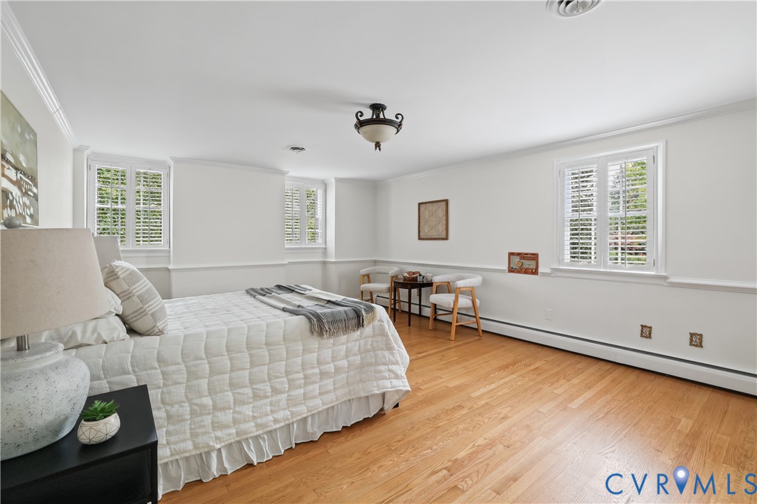 Spacious interior featuring wood-finish flooring, crisp white wall molding, plantation shutters, and a decorative ceiling-mounted light fixture