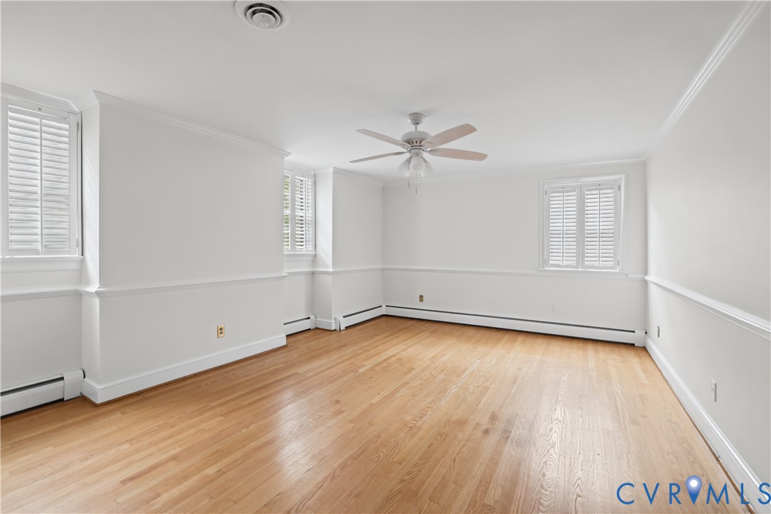 Interior space featuring wood-finish flooring, chair rail molding, shutter-style window treatments, and a ceiling fan with integrated light fixture