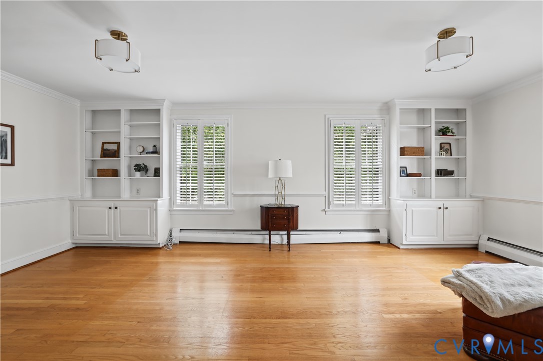 Wood-finish flooring, dual built-in floor-to-ceiling bookshelves with cabinetry, windows featuring white plantation shutters, and dual semi-flush mount drum light fixtures
