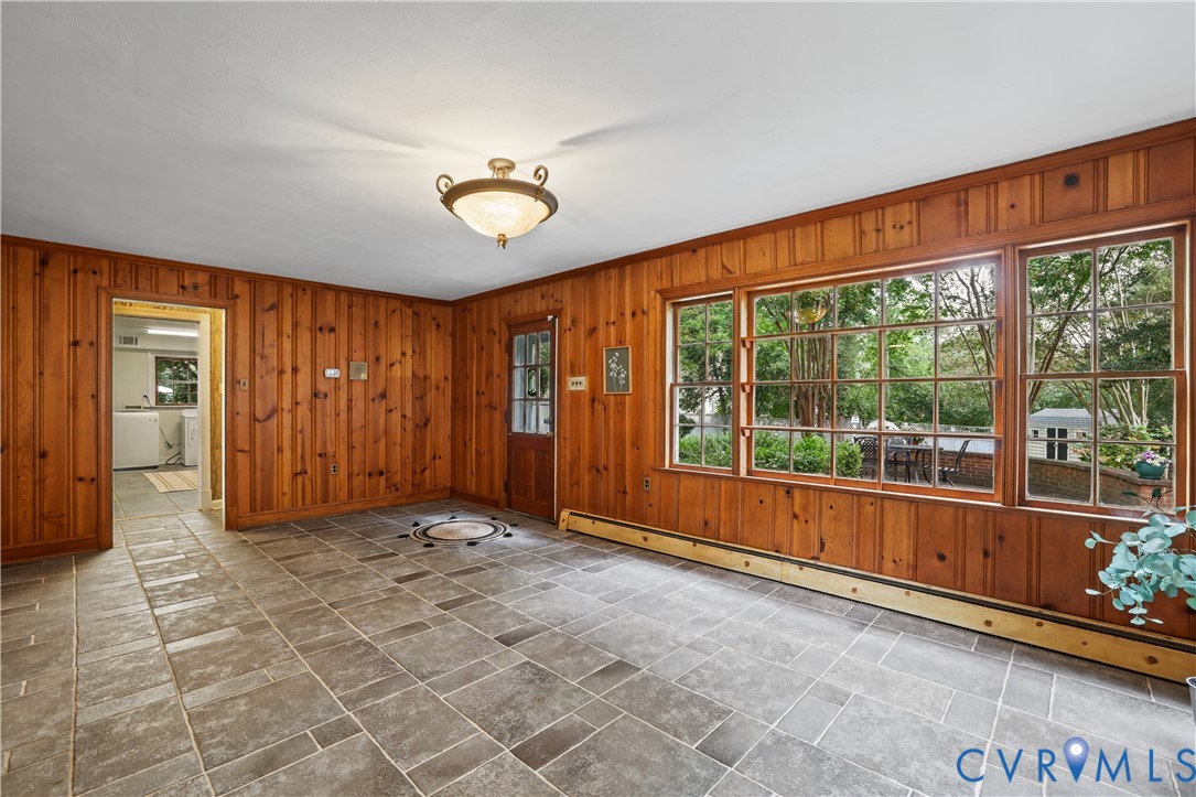 Wood-paneled interior walls, large multi-pane windows, natural stone flooring, a glass-panel wooden entry door, looking into Backyard.