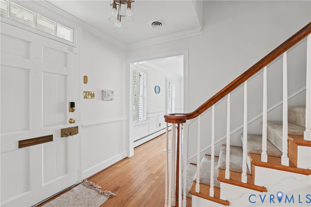 Foyer featuring a paneled front door with transom window, wood-finish flooring, wainscoting, and a staircase with a wooden handrail and white balusters