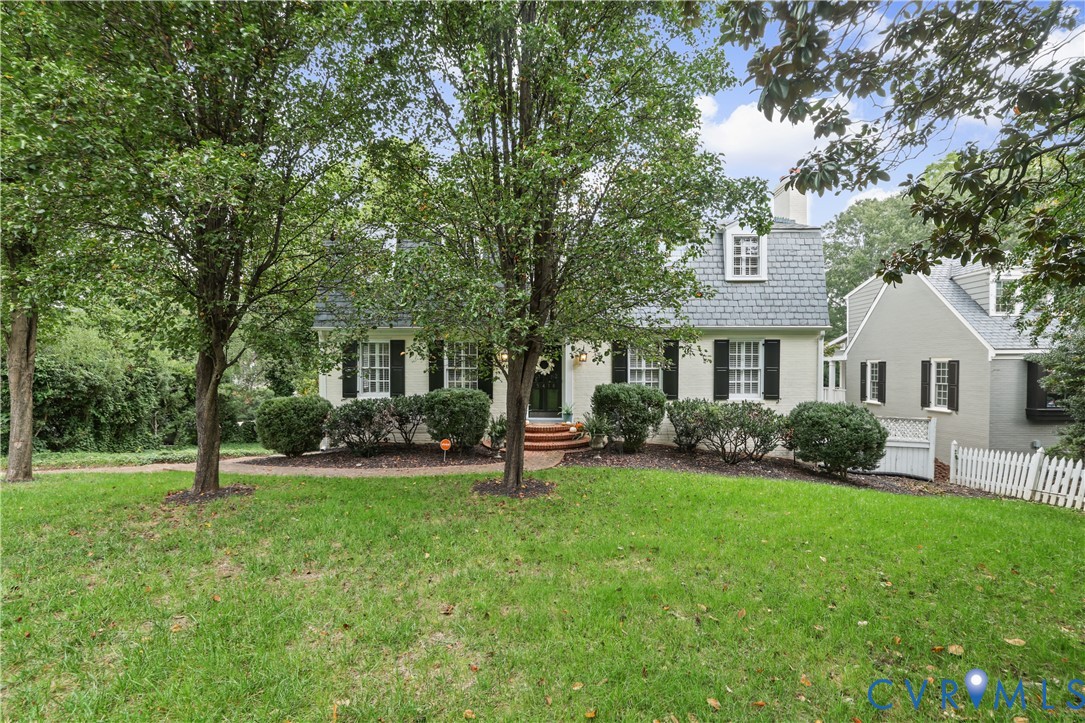 Dutch Colonial exterior featuring a gambrel roof, multi-pane windows with dark shutters, a brick front stoop, and a white picket fence