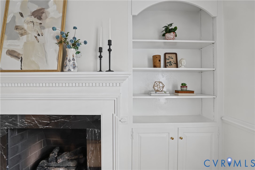 Fireplace featuring a dark stone surround, crown molding, and built-in shelving with lower cabinetry