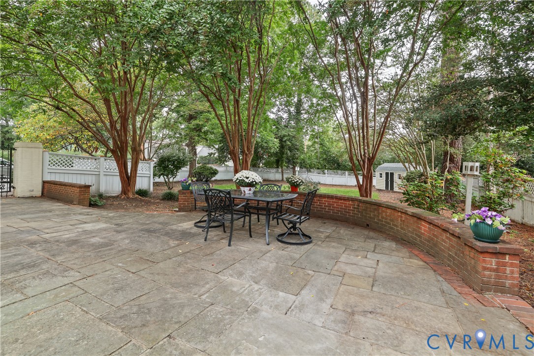 Flagstone patio featuring a curved brick retaining wall, white lattice fencing, and mature trees