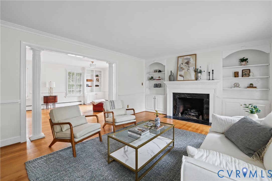 Fireplace with a stone surround, wood-finish flooring, custom built-in cabinetry, and decorative columns