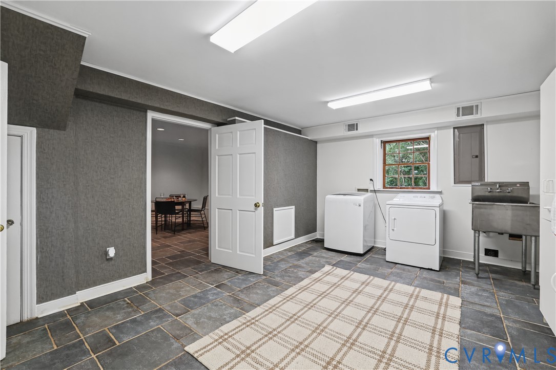 Laundry room featuring stone tile flooring, charcoal-toned walls, and a stainless steel utility sink