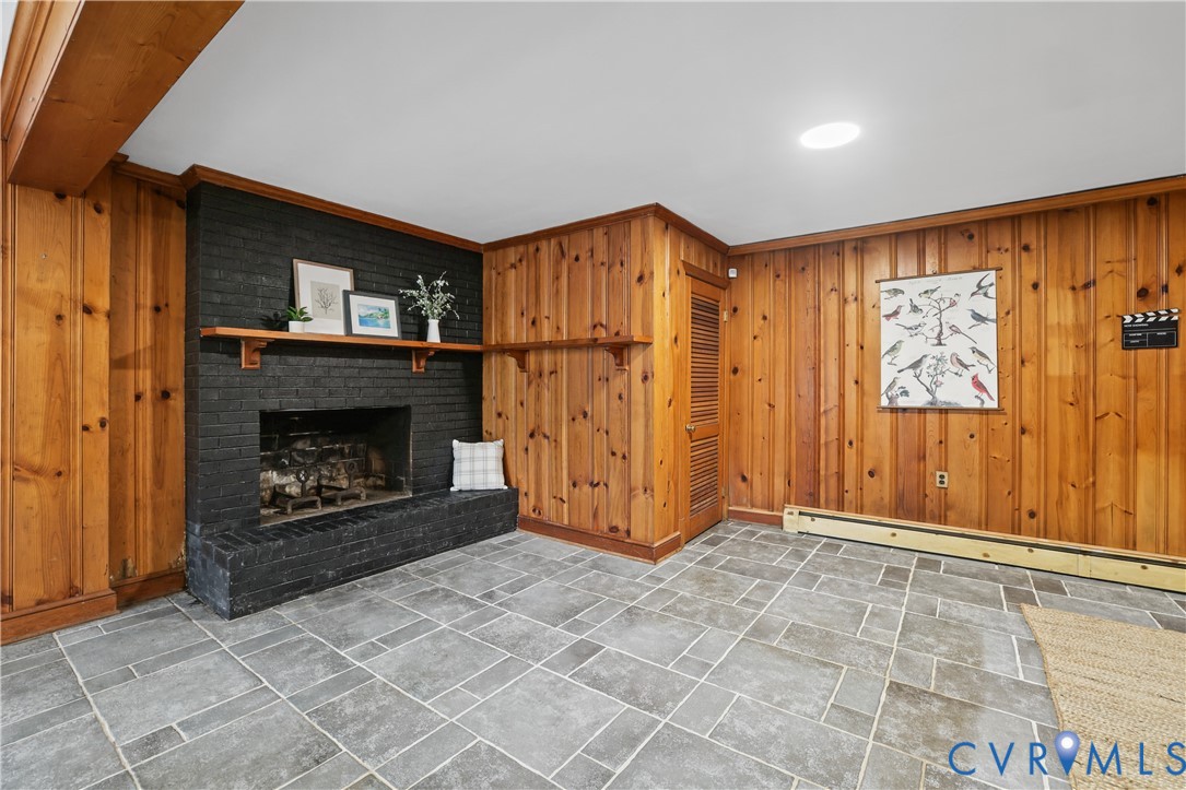 Rec Room featuring knotty wood-panelled walls, a painted brick fireplace with a wood mantel, stone flooring, and a louvered door closet