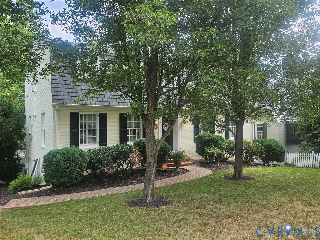 featuring a curved brick pathway, mature trees, and established shrubs
